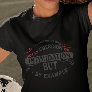 May include: Black t-shirt with a white graphic design that reads "People are changed not by coercion or intimidation but by example."
