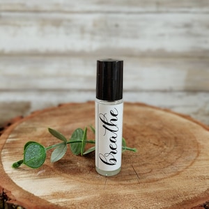May include: A clear glass roller bottle with a black cap and a white label that says "breathe" in black script.
