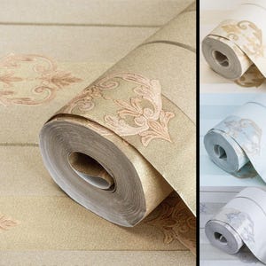May include: A roll of wallpaper featuring a textured gold surface with a repeating damask pattern in a lighter shade. The image also displays three additional rolls of wallpaper in cream, light blue, and white, each with the same damask design.