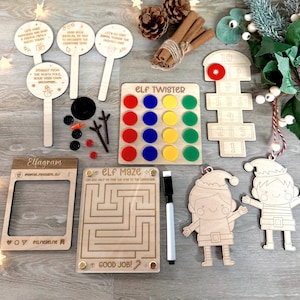 May include: A collection of wooden Christmas-themed activity items including an Elf Twister board with coloured discs, an Elf Maze with a marker, a hopscotch board, three circular signs with text, a photo frame, and two elf-shaped wooden cutouts.