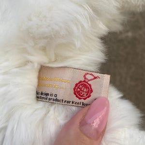 May include: White plush toy with a red and white label that reads "This design is a registered product for Keel Toys".