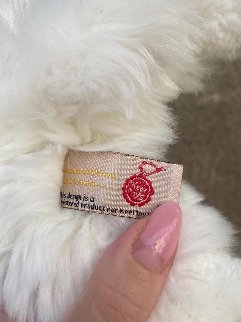 May include: White plush toy with a red and white label that reads "This design is a registered product for Keel Toys".