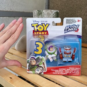 May include: Toy Story 3 Action Links Buddy Pack featuring Buzz Lightyear and a robot. The packaging is blue and red with the Toy Story logo and the Action Links logo.