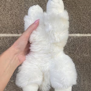 May include: White plush toy shaped like a dog, lying on its back with its paws in the air.