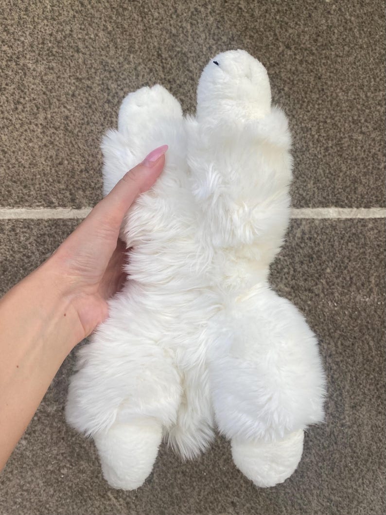 May include: White plush toy shaped like a dog, lying on its back with its paws in the air.