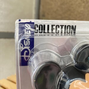 May include: A close-up of a Mickey Mouse figurine in a plastic package. The package is labeled "Disney Collection".