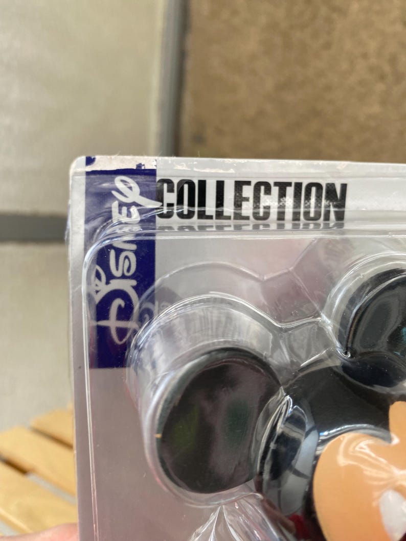 May include: A close-up of a Mickey Mouse figurine in a plastic package. The package is labeled "Disney Collection".