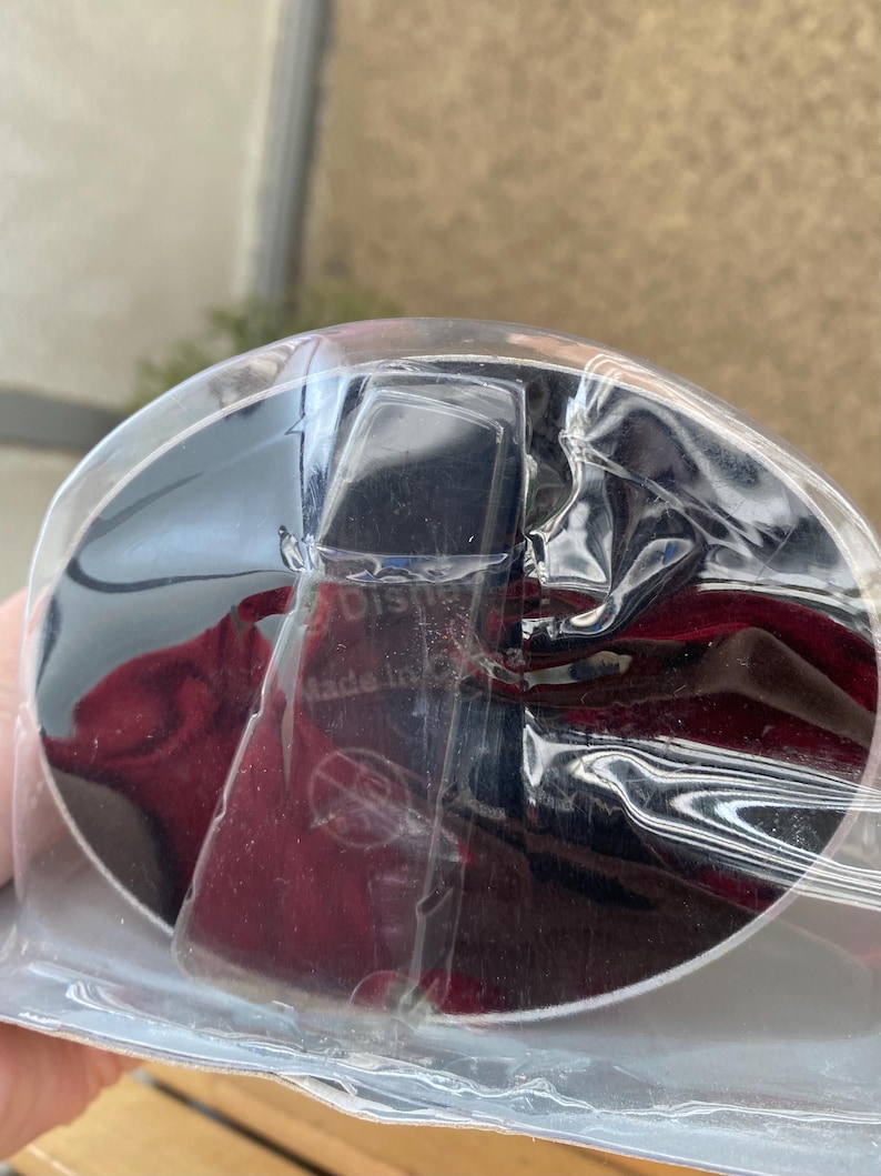 May include: A black and silver round object with a red and black background. The object is wrapped in clear plastic and has the text "Made in China" printed on it.