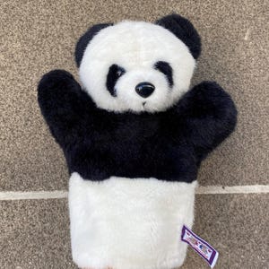 Könnte beinhalten: Handpuppe in Panda-Form aus schwarz-weißem Plüschstoff. Die Puppe hat schwarze Augen, Ohren und Arme, mit einem weißen Gesicht und Bauch. Ein kleines Etikett ist am Handgelenk befestigt. Zum Spielen über die Hand zu ziehen.