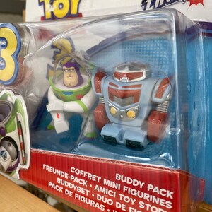 May include: Toy Story Action Links Buddy Pack featuring Buzz Lightyear and a robot. The packaging is red and blue with the Toy Story logo and the words "Action Links" in large letters.
