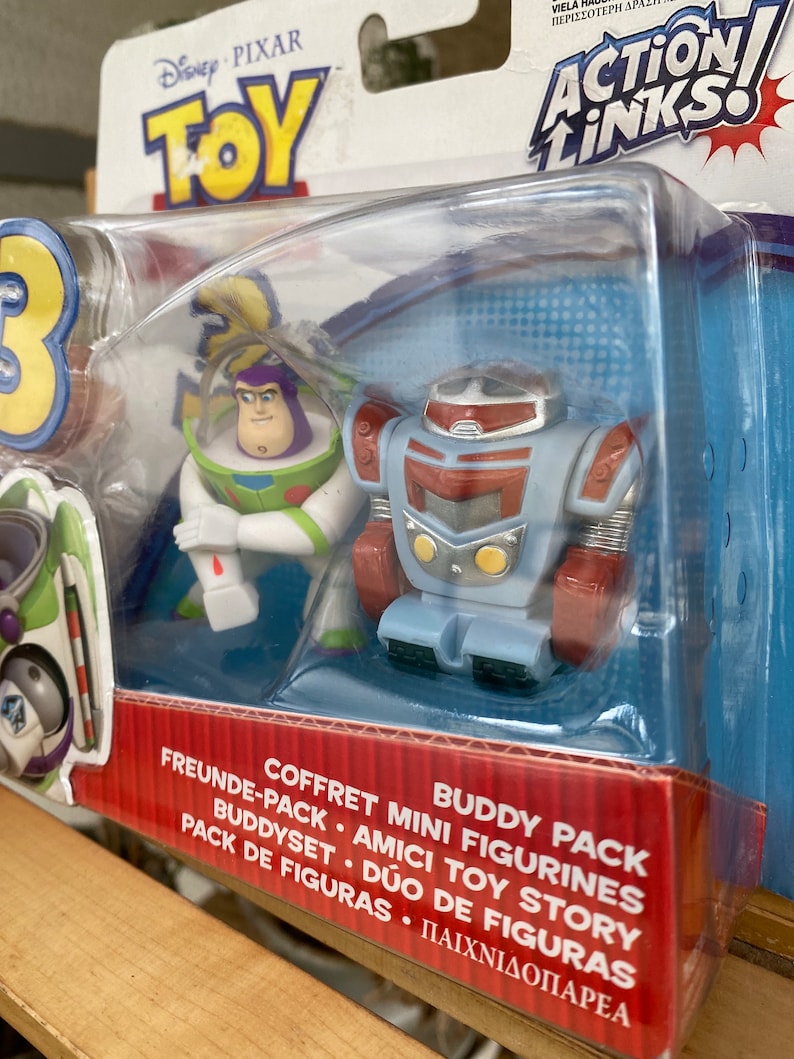 May include: Toy Story Action Links Buddy Pack featuring Buzz Lightyear and a robot. The packaging is red and blue with the Toy Story logo and the words "Action Links" in large letters.