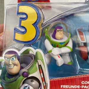 May include: A plastic package with a Toy Story 3 theme featuring three small figures of Buzz Lightyear. The figures are in different poses and include a Buzz Lightyear figure in his space ranger suit, a Buzz Lightyear figure in his space ranger suit with a jetpack, and a Buzz Lightyear figure in his space ranger suit with a helmet. The package also includes the text "Freunde-Pac Buddies Pack de Fig"