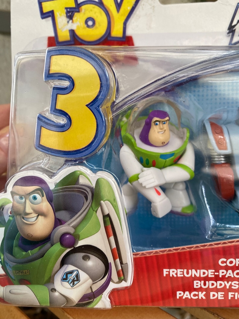 May include: A plastic package with a Toy Story 3 theme featuring three small figures of Buzz Lightyear. The figures are in different poses and include a Buzz Lightyear figure in his space ranger suit, a Buzz Lightyear figure in his space ranger suit with a jetpack, and a Buzz Lightyear figure in his space ranger suit with a helmet. The package also includes the text "Freunde-Pac Buddies Pack de Fig"