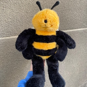 May include: A plush bee toy with black and yellow stripes. The bee has black antennae, black legs, and a fuzzy yellow body.
