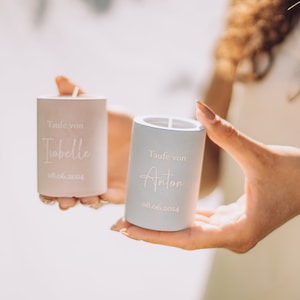 Op de afbeelding: Twee kleine, cilindrische kaarsen met witte letters. De roze kaars heeft de tekst "Taufe von Isabelle 08.06.2024" en de blauwe kaars "Taufe von Anton 08.06.2024".