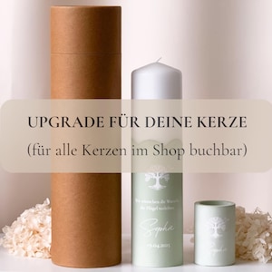 Puede incluir: Una vela blanca con una etiqueta verde que dice "Upgrade für deine Kerze (für alle Kerzen im Shop buchbar)". La etiqueta también tiene un diseño de árbol y el nombre "Sophie" con una fecha. Hay un tubo de cartón marrón y una vela verde más pequeña con un diseño de árbol.