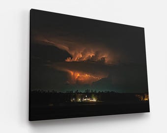 May include: A dark, stormy night sky with a single bolt of lightning illuminating the clouds. The clouds are a vibrant orange and yellow, contrasting with the dark blue sky. A silhouette of trees and a house are visible in the distance.