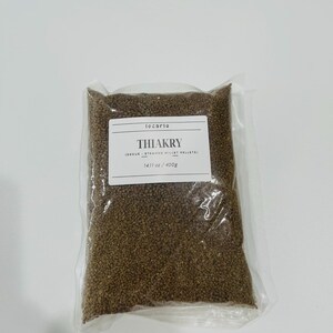 May include: A clear plastic vacuum-sealed bag containing brown steamed millet pellets. A white rectangular label on the front reads locario THIAKRY (DEGUE - STEAMED MILLET PELLETS) 14.11 oz / 400g in black text with horizontal lines above and below.