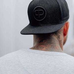 Könnte beinhalten: Eine schwarze Baseballkappe mit einem großen, geprägten, schwarzen Kreislogo mit den Buchstaben "CP".
