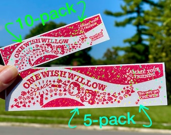May include: Two rectangular stickers with a pink glitter finish featuring the text ONE WISH WILLOW, AMAZE YOUR FRIENDS, and You only get ONE WISH. The design includes illustrations of two faces, stars, and the word CRACK in a bold font.