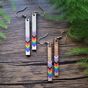 May include: A pair of wooden earrings with a rainbow chevron pattern. The earrings are made of natural wood and have silver hooks.