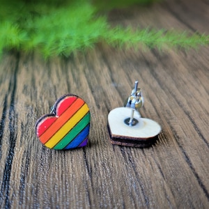 Könnte beinhalten: Ein Paar regenbogenförmige Ohrringe in Herzform. Ein Ohrring ist ein Regenbogenherz, der andere ein schlichtes Holzhertz mit einem silbernen Stift.