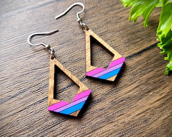 May include: A pair of wooden earrings with a geometric triangle shape. The earrings are painted with stripes of pink, blue, and purple.