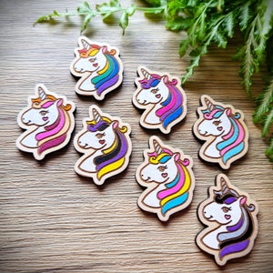 May include: Eight wooden unicorn head ornaments with different colored manes and horns. The unicorns are painted in shades of pink, purple, blue, yellow, black, and grey.
