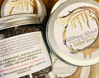 May include: A silver jar of coffee scrub with a black and white label that reads "Willow Wood Farm & Apothecary Coffee Scrub". The label also includes a description of the product's benefits and ingredients, including Maine roasted ground coffee, organic sugar, and vitamin E oil.