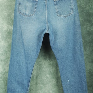 Peut inclure: Un jean en denim bleu clair avec un &eacute;cusson en cuir brun sur lequel est inscrit "Wrangler" au dos.