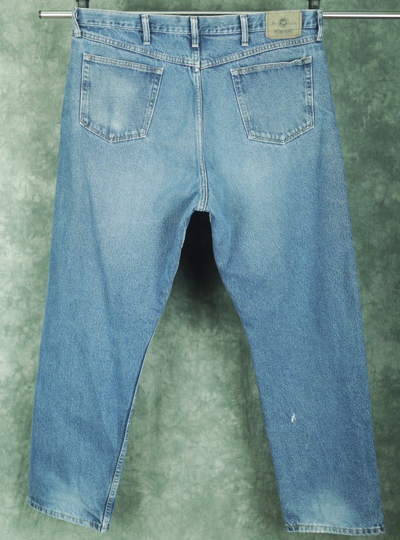 Peut inclure: Un jean en denim bleu clair avec un &eacute;cusson en cuir brun sur lequel est inscrit "Wrangler" au dos.