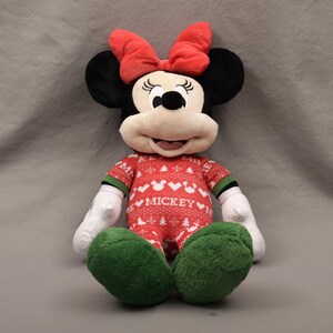 May include: A plush Minnie Mouse doll with a red bow, black ears, and a red and white patterned outfit. The outfit has the word "Mickey" on it. The doll has green feet and white gloves.