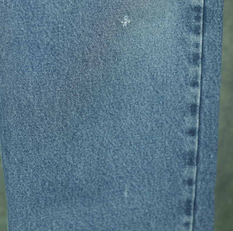 Peut inclure: Gros plan sur un tissu en jean bleu avec une texture subtile. Le tissu a une couture qui descend sur le c&ocirc;t&eacute; droit.