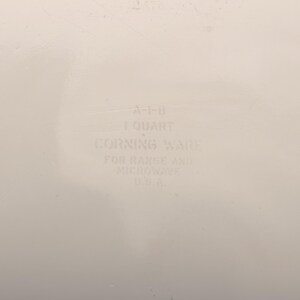 May include: Off-white Corning Ware dish with text that reads "A-1-B 1 QUART CORNING WARE FOR RANGE AND MICROWAVE U.S.A.". The dish is designed for use in both the range and microwave.