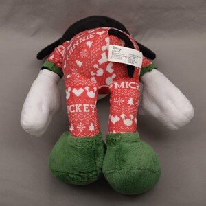 May include: A Mickey Mouse plush toy, viewed from the back, wearing a red and white patterned outfit with the word "Mickey" on the legs. The plush has black ears, white gloves, and green shoes. A Disney tag is visible.