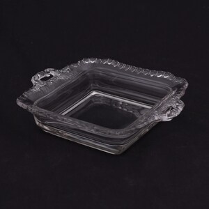 May include: A clear glass square dish with two handles. The dish has a decorative, scalloped edge.