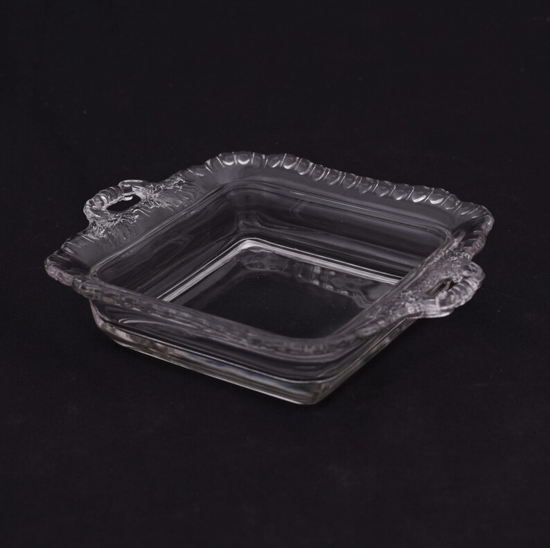 May include: A clear glass square dish with two handles. The dish has a decorative, scalloped edge.