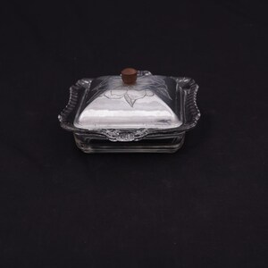 May include: A clear glass butter dish with a silver-plated lid and a wooden knob. The lid has a floral design etched into it.