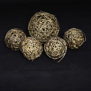 May include: A collection of five decorative spheres crafted from interwoven twigs with a metallic gold finish. The set includes one large central sphere surrounded by four smaller spheres, all featuring a complex, open-weave lattice structure.