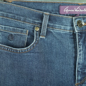 May include: Close-up of a pair of blue denim jeans with a brown leather patch on the front pocket and a purple label that reads "Gloria Vanderbilt".