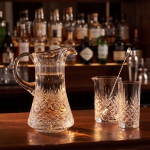 May include: A clear glass pitcher with a faceted diamond-cut pattern, a matching mixing glass, and a long twisted metal bar spoon. The pitcher features a wide handle and a pouring spout, while the glasses display intricate geometric detailing.