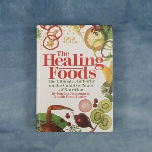 May include: A hardcover book titled "The Healing Foods" with a white cover and red lettering. The cover features illustrations of various fruits and vegetables. The book's subtitle reads "The Ultimate Authority on the Curative Power of Nutrition."