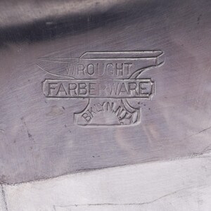May include: Close-up of a silver metal object with the words "Wrought Farberware Brooklyn NY" embossed on it.