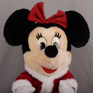 Pu&ograve; includere: Un peluche di Minnie Mouse con orecchie nere, un fiocco rosso e un vestito rosso e bianco. Il personaggio ha grandi occhi, un naso nero e un sorriso rosso. Il peluche &egrave; progettato per assomigliare all'iconico personaggio Disney.
