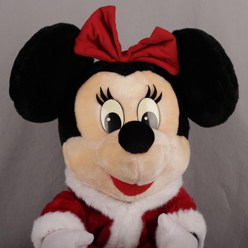 Pu&ograve; includere: Un peluche di Minnie Mouse con orecchie nere, un fiocco rosso e un vestito rosso e bianco. Il personaggio ha grandi occhi, un naso nero e un sorriso rosso. Il peluche &egrave; progettato per assomigliare all'iconico personaggio Disney.