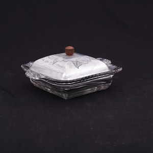 May include: A clear glass butter dish with a wooden knob on the lid. The dish has a floral design etched into the glass.