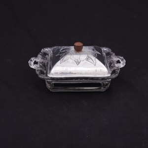 May include: A clear glass butter dish with a silver lid and a wooden knob. The lid has a floral design etched into it.