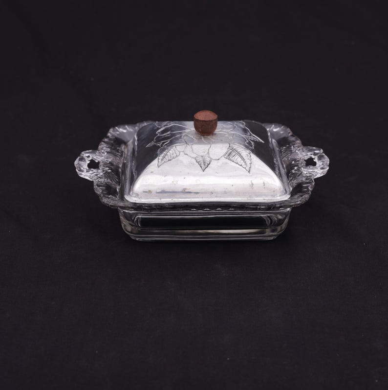 May include: A clear glass butter dish with a silver lid and a wooden knob. The lid has a floral design etched into it.
