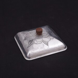 May include: A silver square box with a floral design and a wooden knob on the lid.