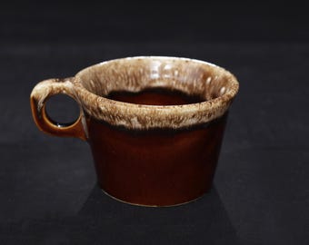 May include: A ceramic mug featuring a deep brown base color that transitions into a lighter, creamy beige drip glaze around the upper rim and handle. The cup has a wide, open mouth and a sturdy, rounded side handle for gripping.